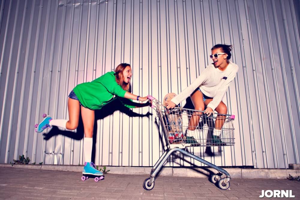 two beautiful young girls with a scateboard, roller scates and a supermarket trolley